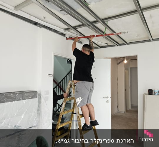 אדם על סולם מתקין צינור תקרה אדום